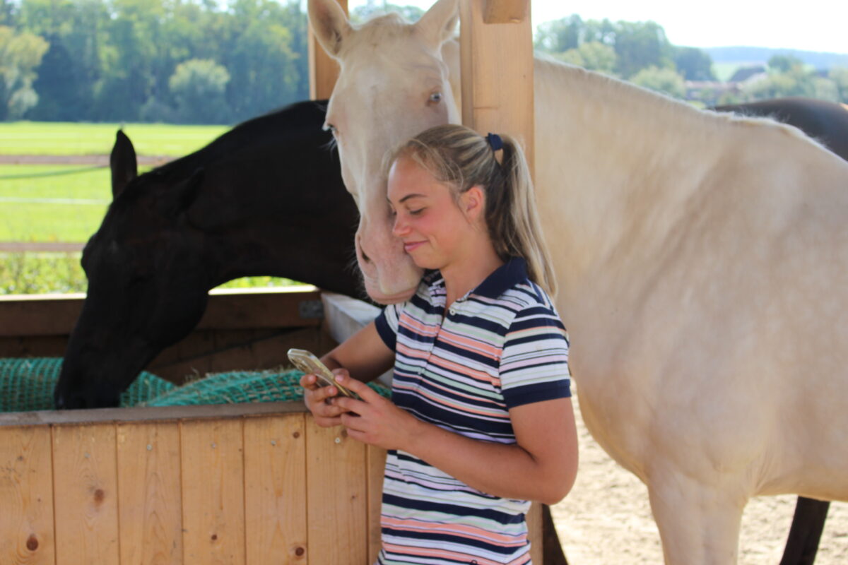 Stallbetreiberin am Pferd mit dem Smartphone